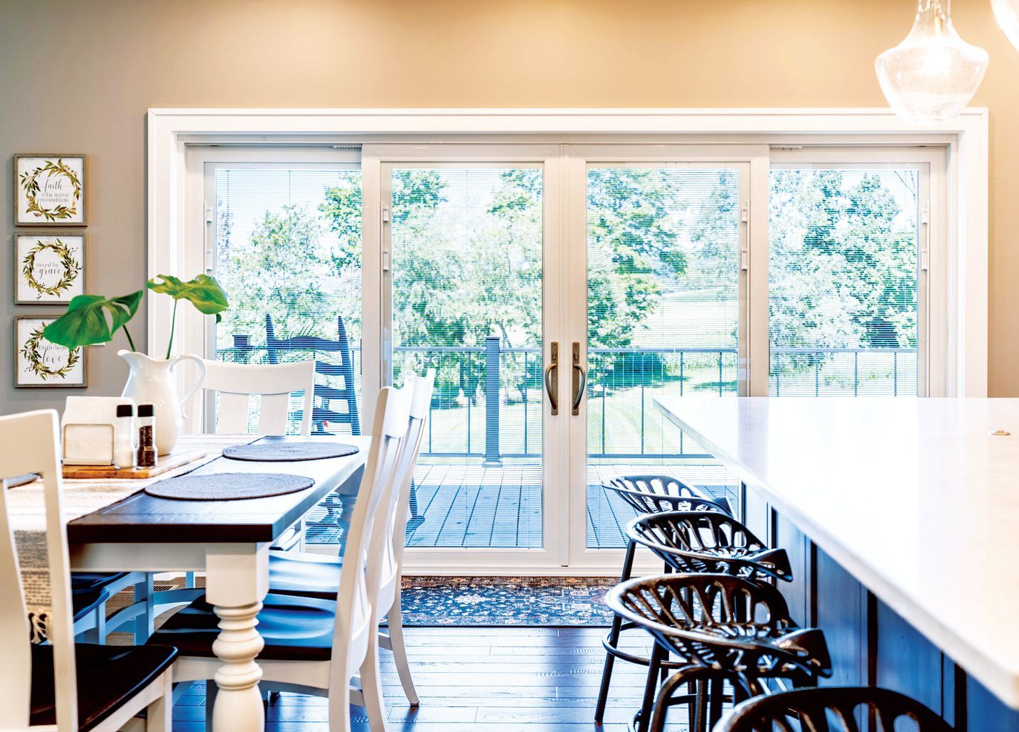 A bright dining area featuring a wooden table with white chairs and a modern kitchen island with black stools by patio doors.