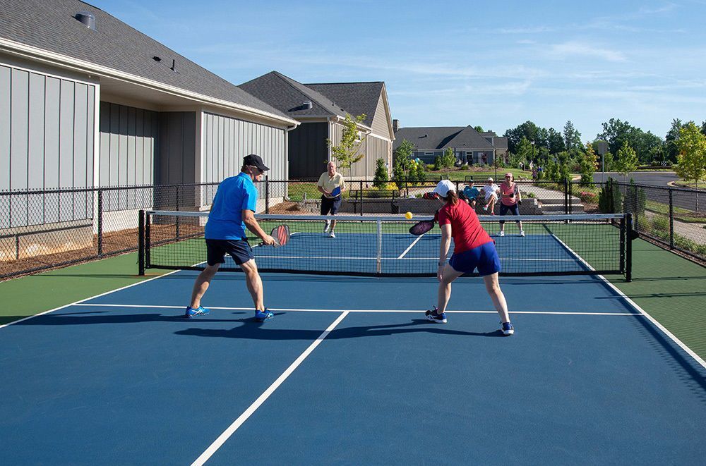 Two people play pickleball on a blue court with a net, with spectators in the background.