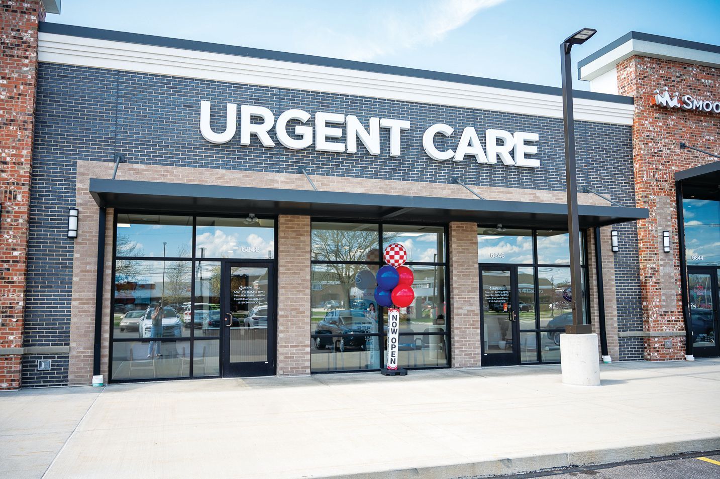 An Urgent Care medical center exterior with brick accents, glass doors, and a small cluster of red and blue balloons.