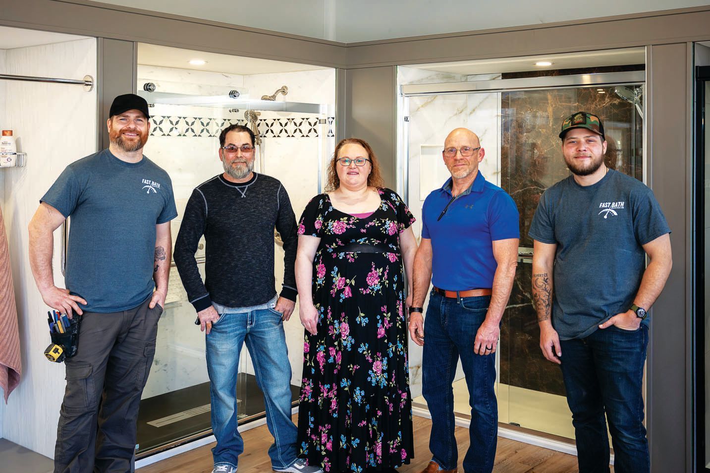 Five people stand in a professional showroom with tiled shower displays behind them.