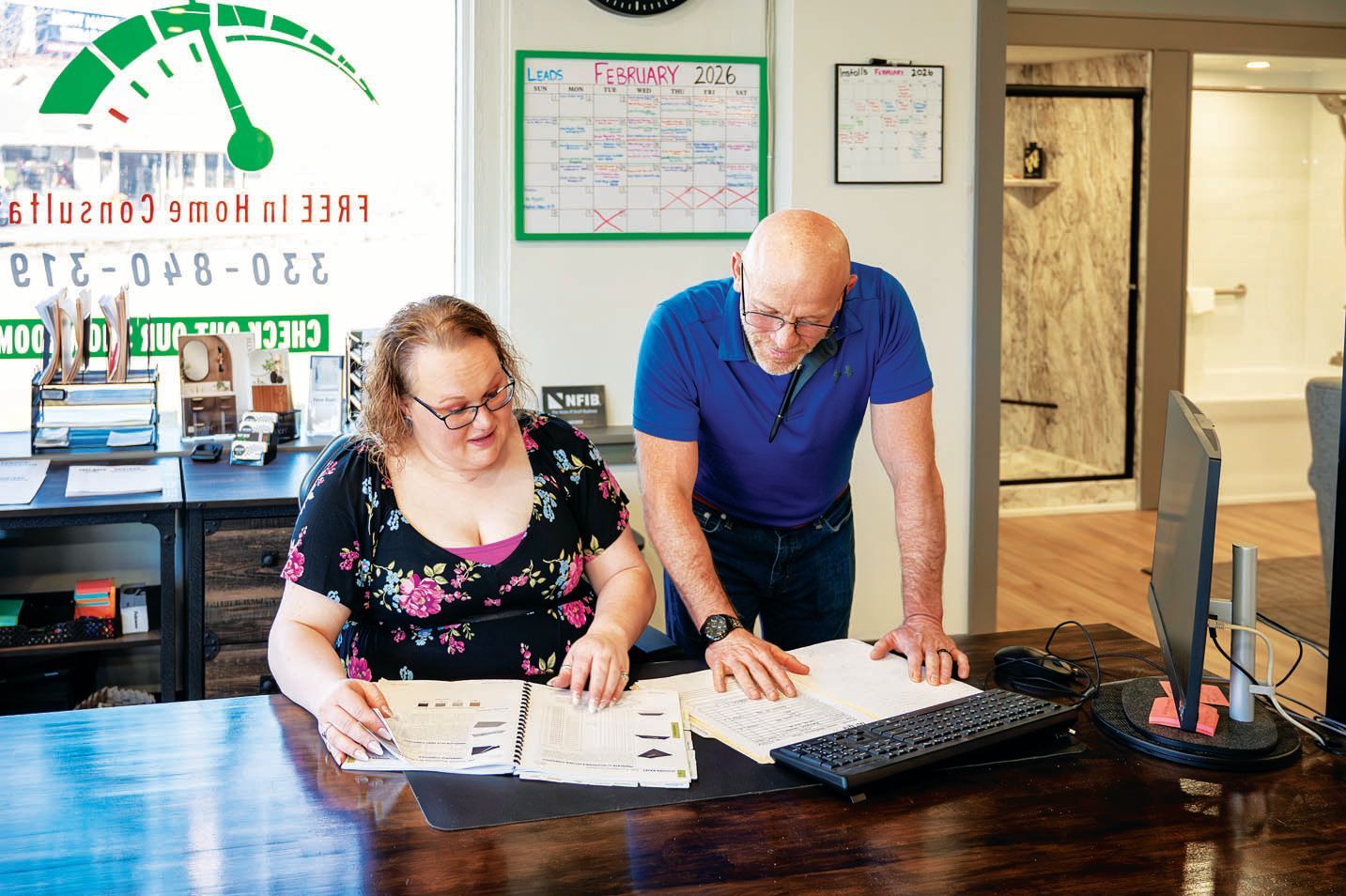 Two people in an office review documents together at a dark wooden desk.