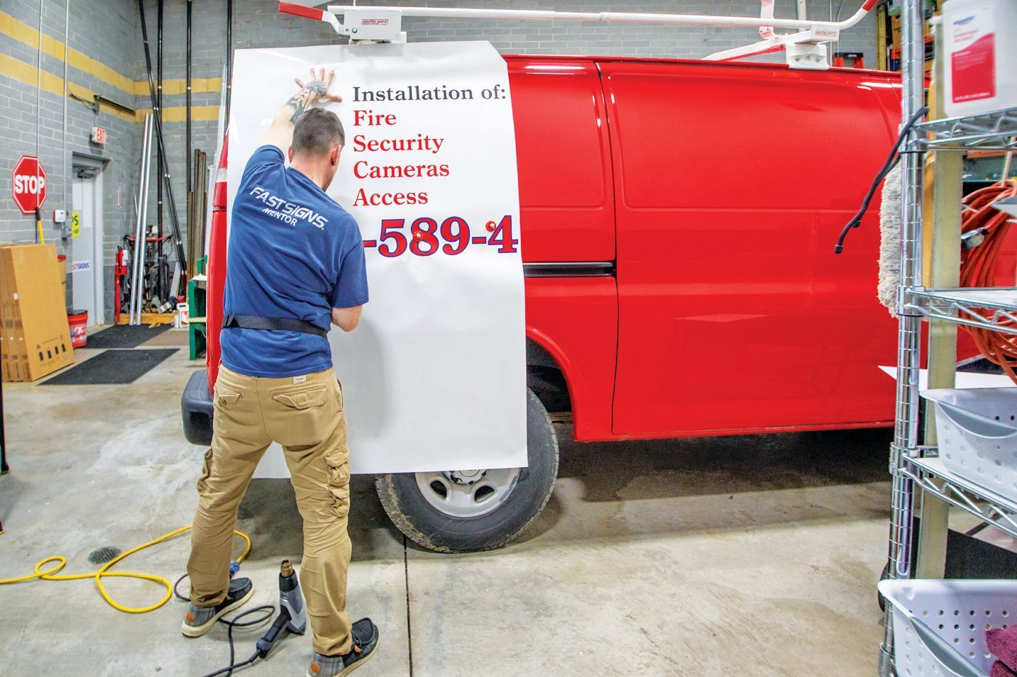 A person applies a decal for a fire and security company to the side of a red van in a garage.