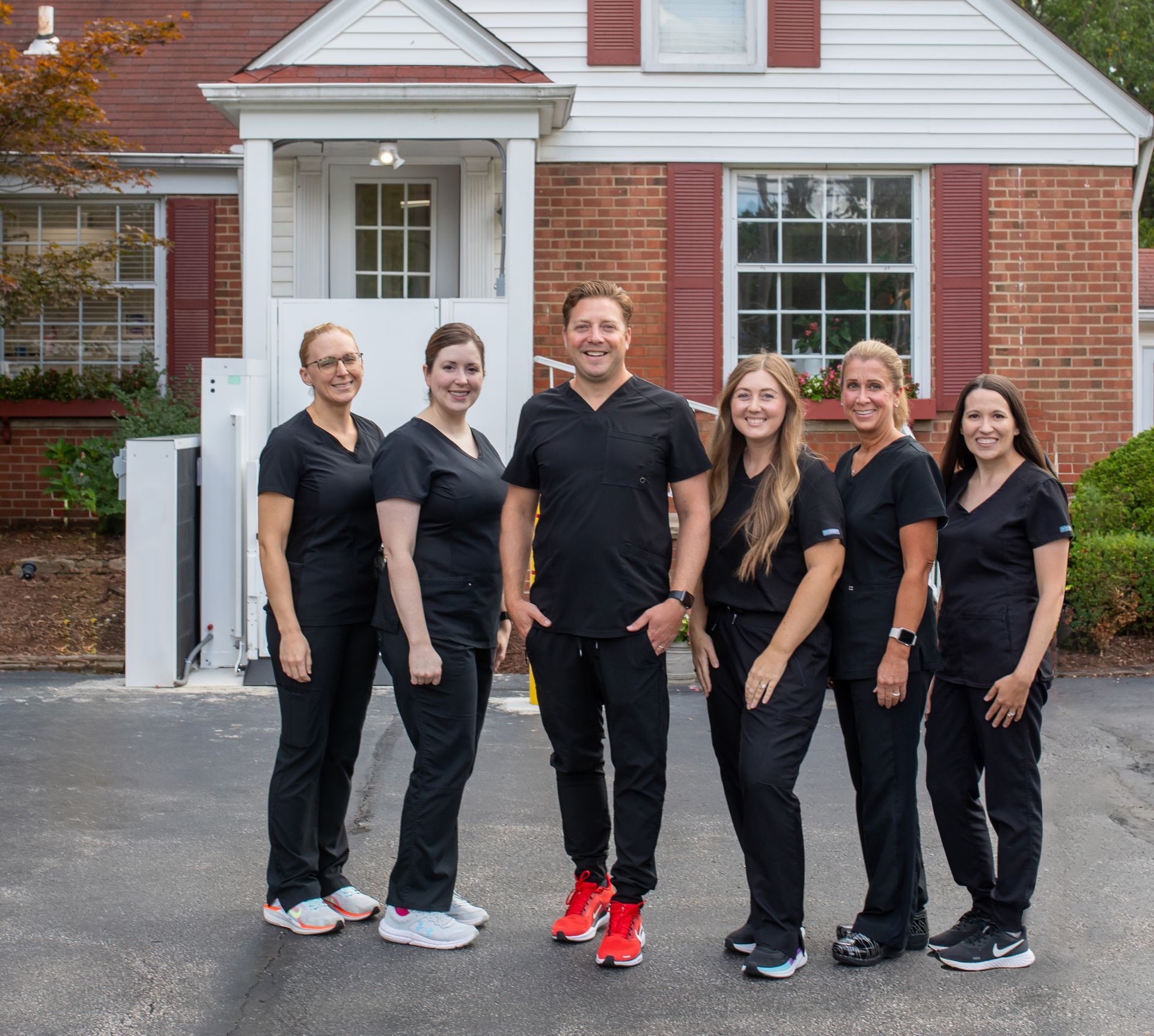 A dental or medical team in matching black scrubs standing in a row outside a brick building.