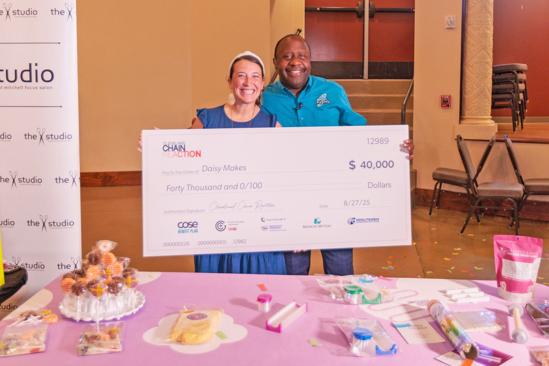 Two people smile while holding a large $40,000 ceremonial check during an event held in front of a branded backdrop.