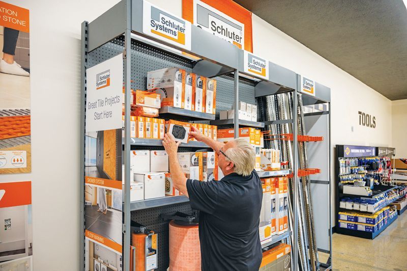 A person in a dark shirt browses Schluter Systems tile installation products on store shelves.