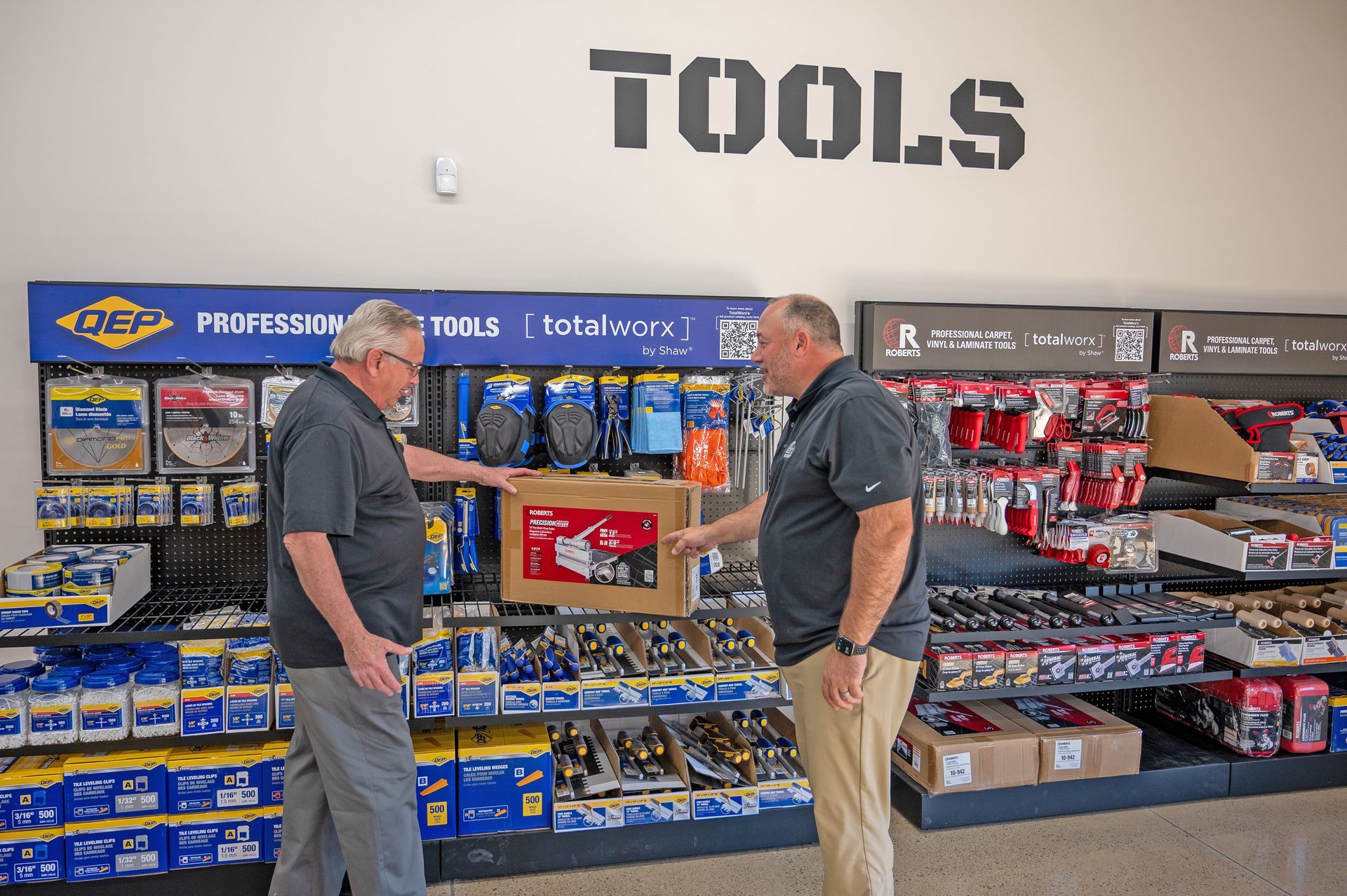 Two professionals stand in a retail aisle, discussing a QEP branded tool box in a store section labeled 
