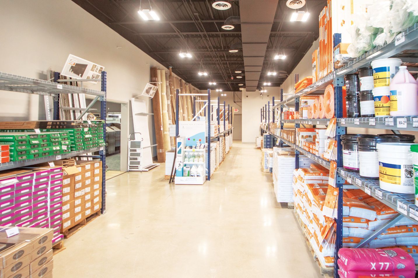 An aisle in a hardware or supply store featuring metal shelving units filled with various packaged products and materials.