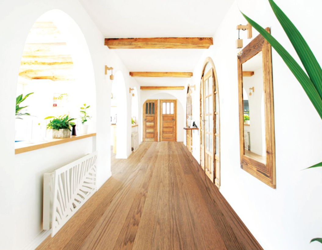 A bright, white hallway with wooden floors, arched doorways, rustic beams, and a mirror on the wall.