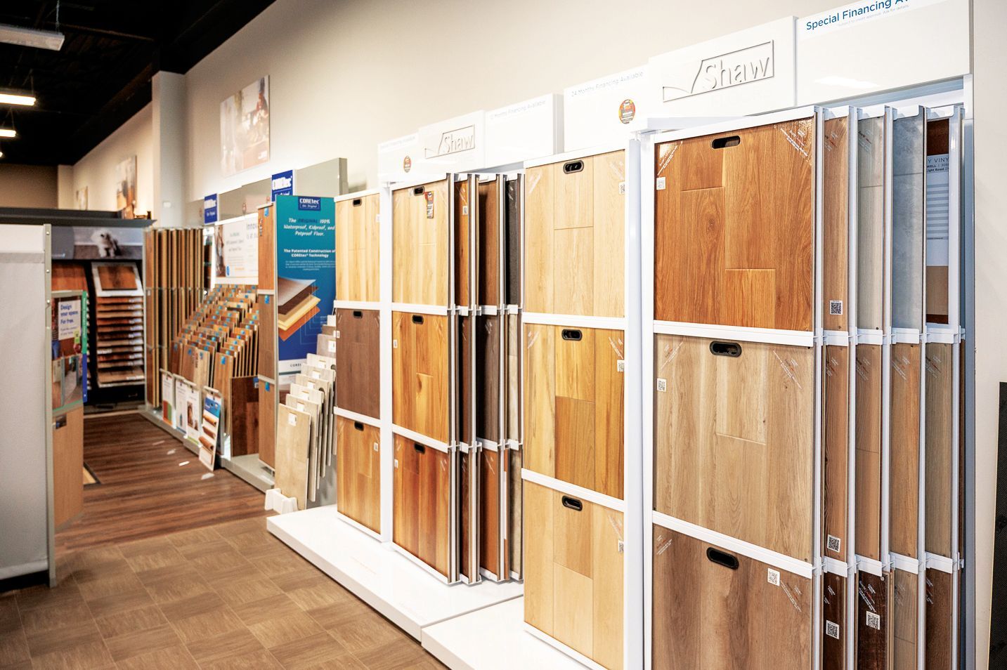 A showroom aisle displaying various wood and laminate flooring samples organized on metal vertical racks.
