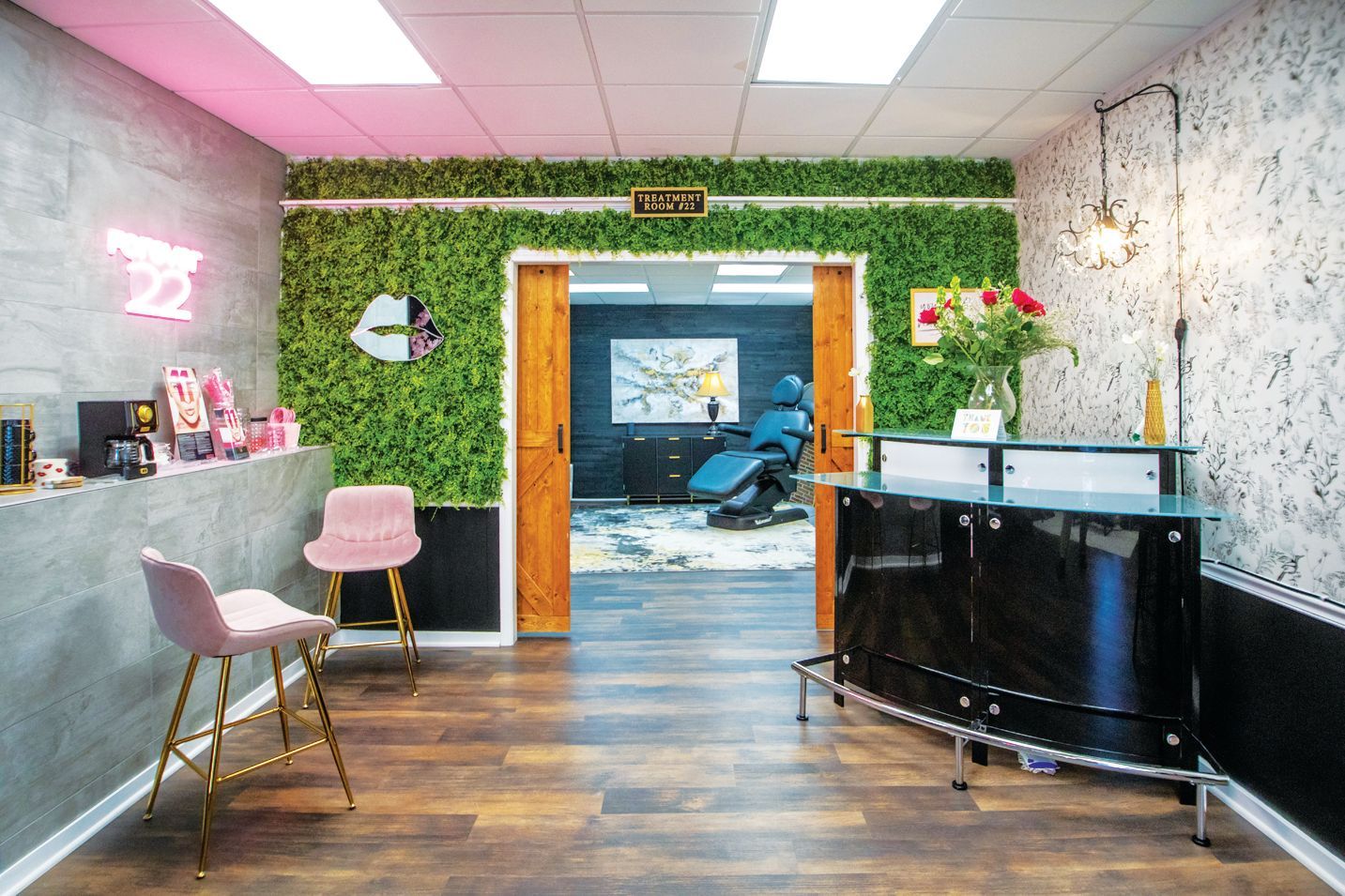 An inviting reception area for a beauty studio with pink stools, a green plant wall, and a black front desk.