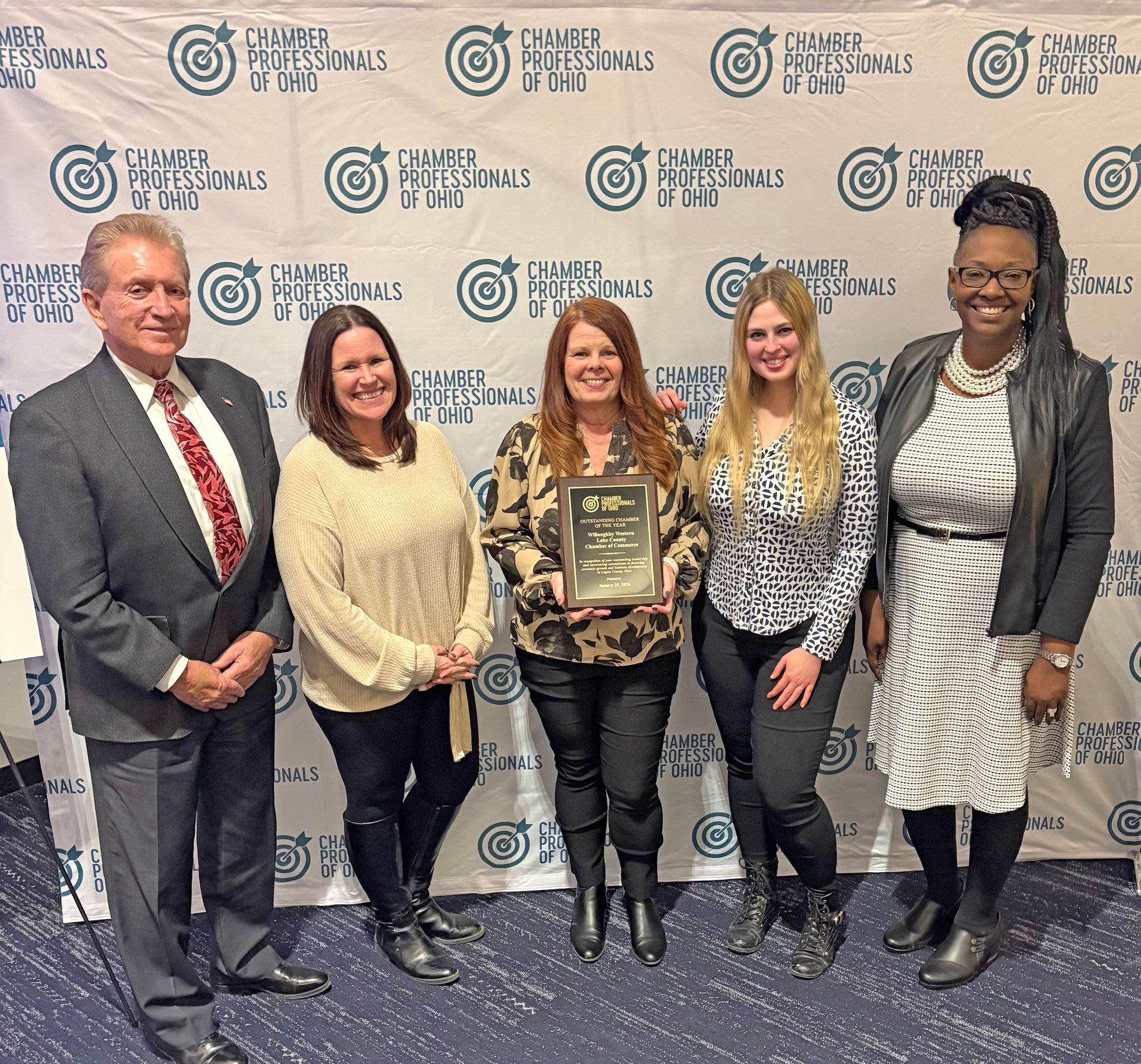 Five people stand in front of a branded backdrop holding an award plaque at a Chamber Professionals of Ohio event.