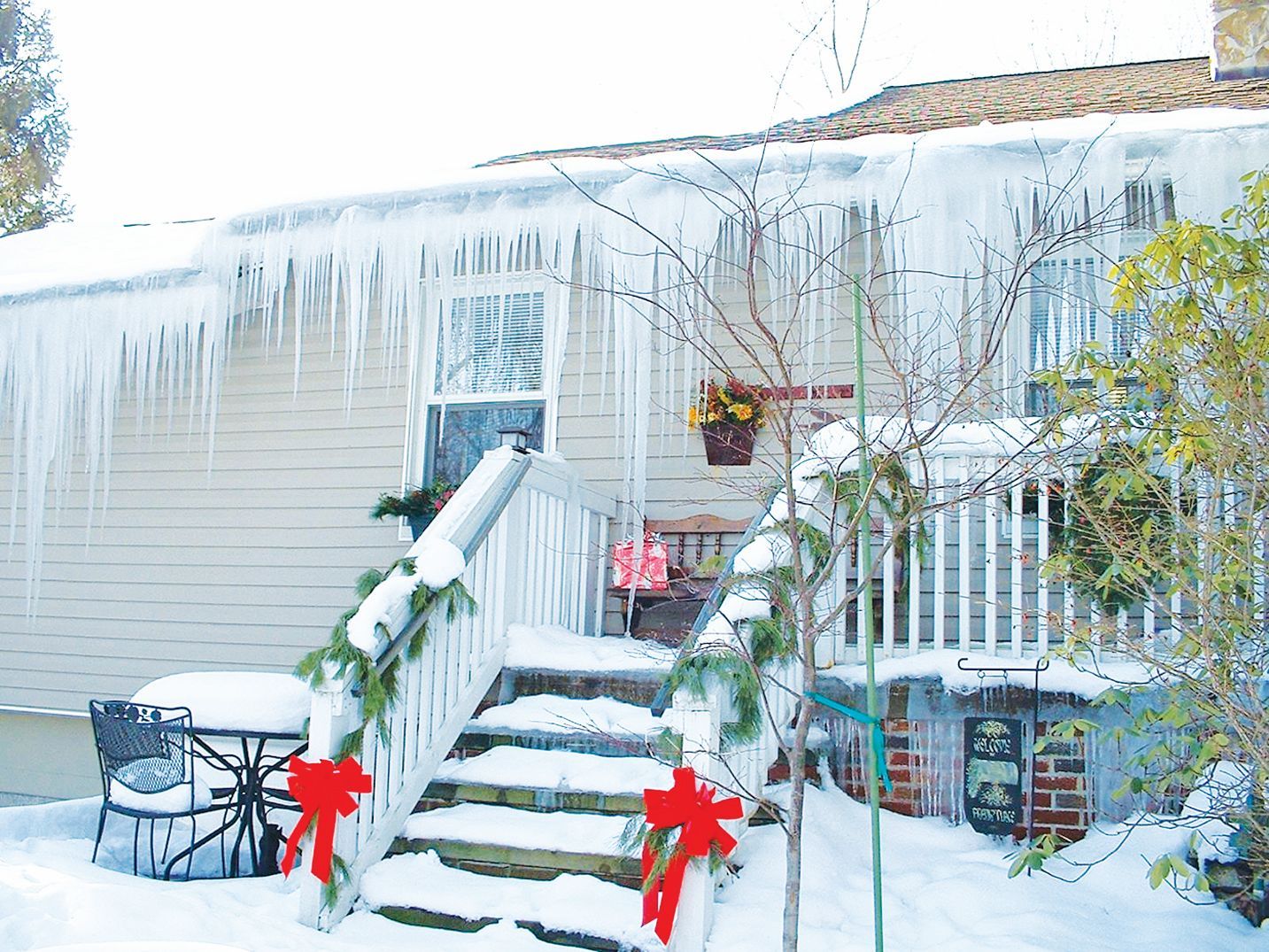 A house porch decorated for the holidays covered in heavy snow and large icicles hanging from the roof.