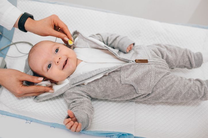 A clinician performs a hearing screening on an infant by holding a sensor against the baby's ear.