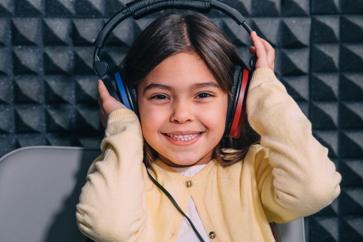 A smiling child wearing headphones sits in front of sound-absorbing foam wall panels.