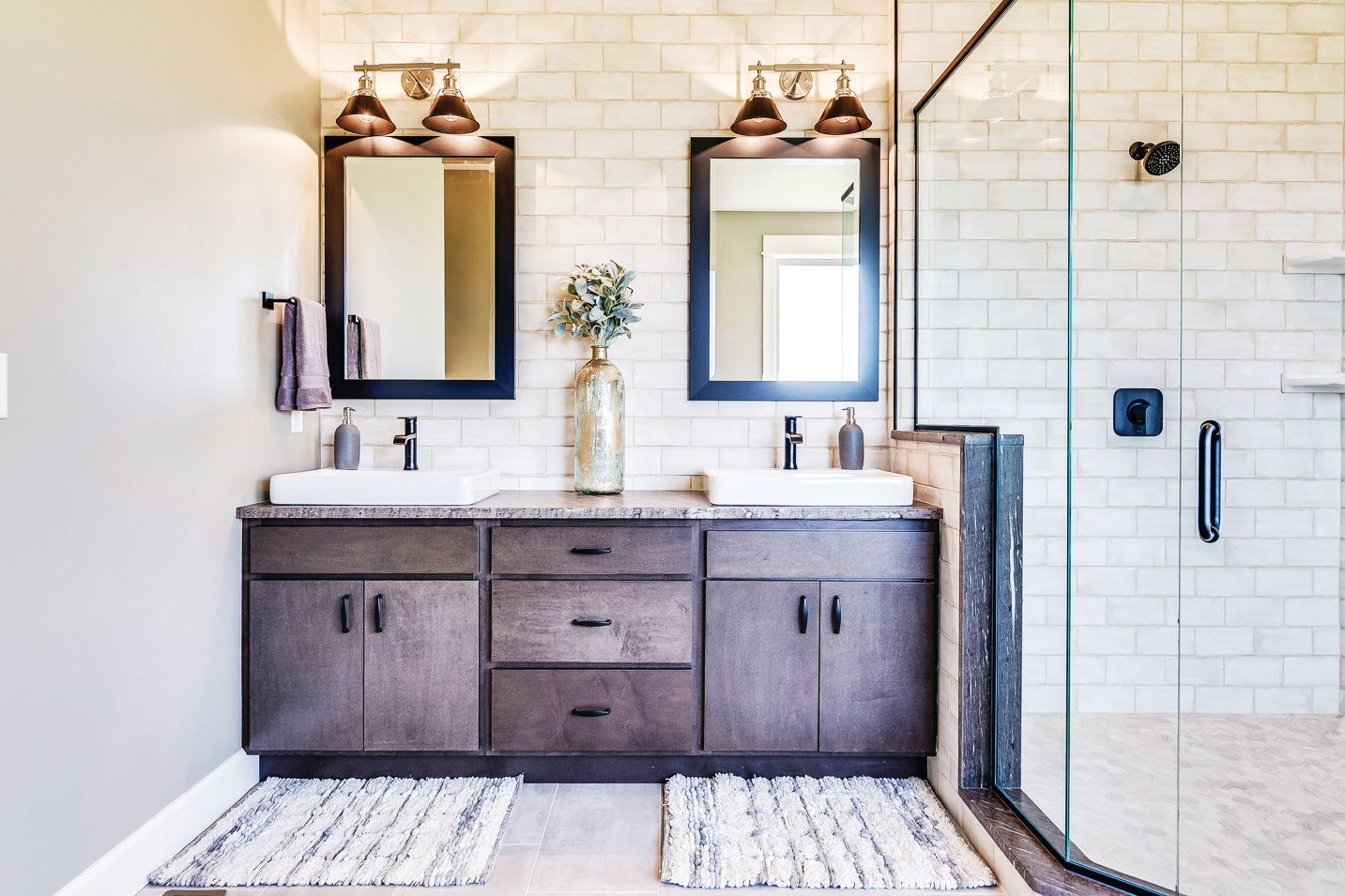 Double-sink bathroom vanity with dark wood cabinets, white subway tile backsplash, and a glass-enclosed shower.