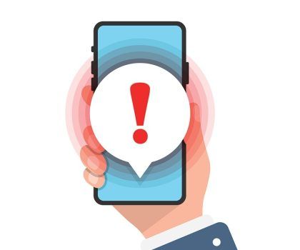A hand holds a smartphone displaying a speech bubble with a red exclamation mark, suggesting an alert or notification.