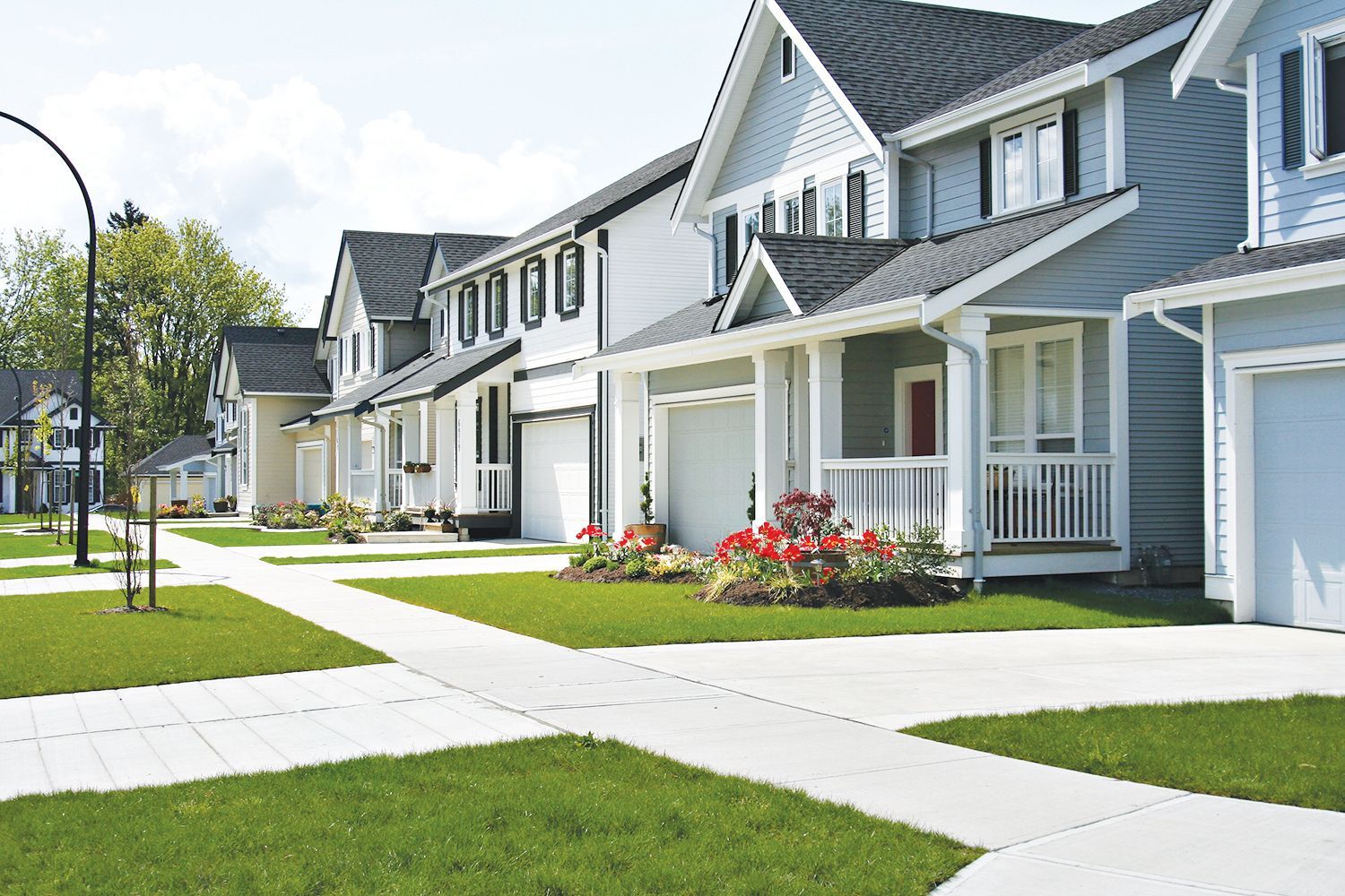 A row of modern, blue and white suburban homes with gray roofs and manicured lawns on a sunny day.