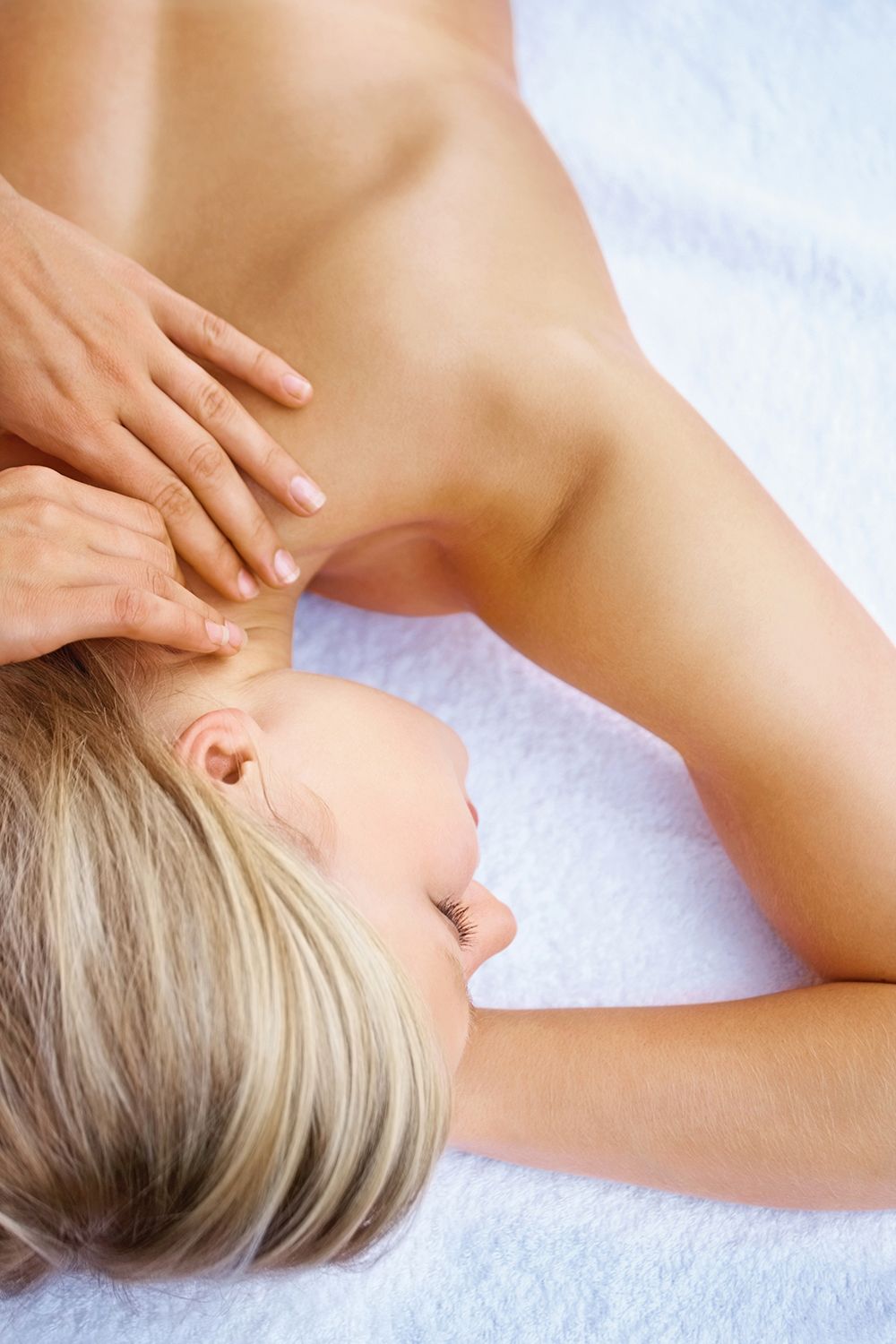 A person lying on a white towel receives a relaxing shoulder and neck massage.