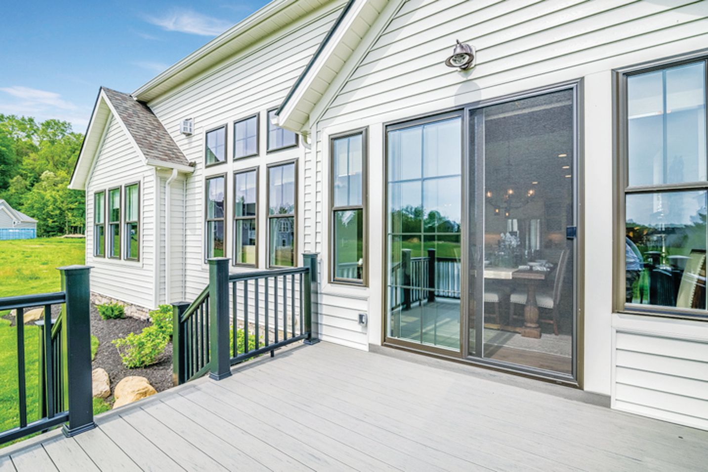 Light-colored house exterior with a gray deck, black railings, and a large sliding glass door overlooking a grassy lawn.