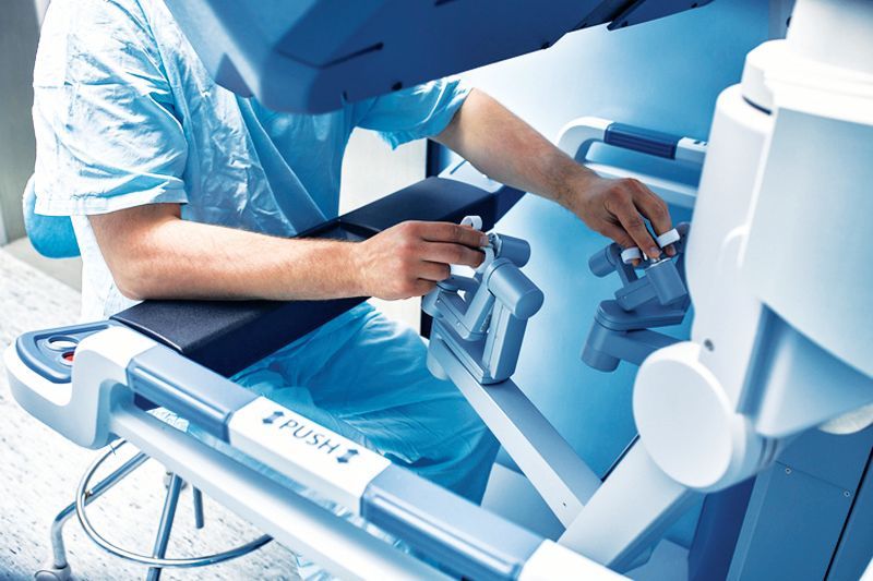 A surgeon operating a robotic surgical system, using handheld controllers to manipulate instruments from a console.