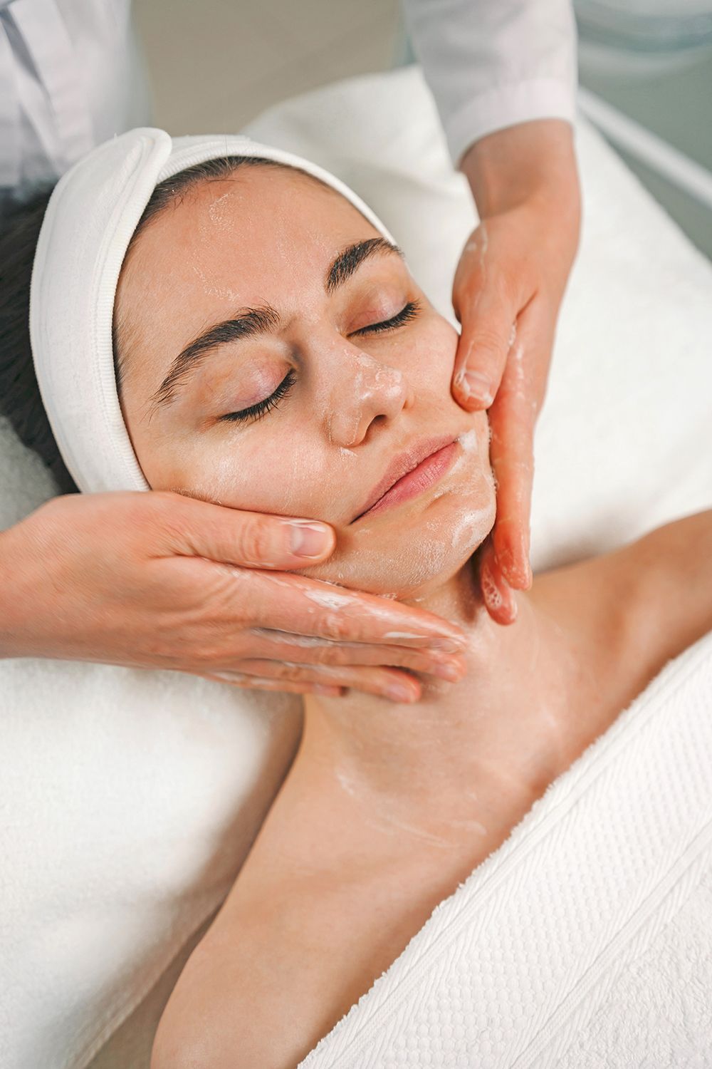 A professional aesthetician performs a facial massage on a person receiving a spa treatment.
