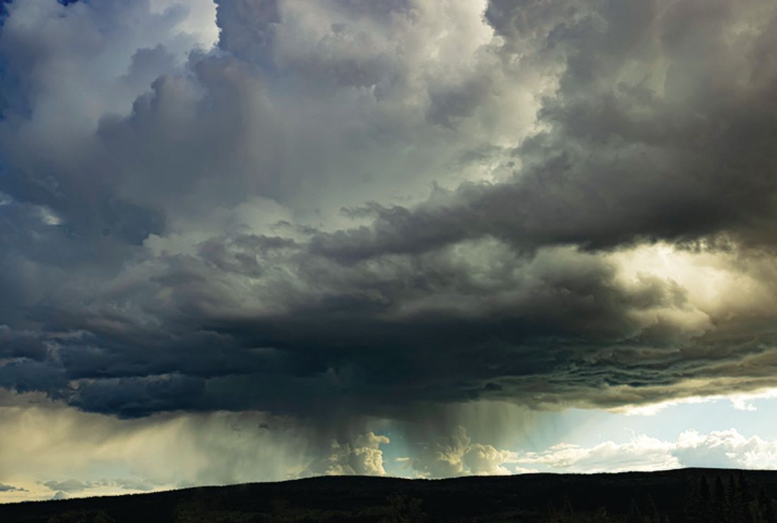 A dark, heavy storm cloud hangs over a distant horizon, with streaks of rain falling toward the silhouetted landscape.