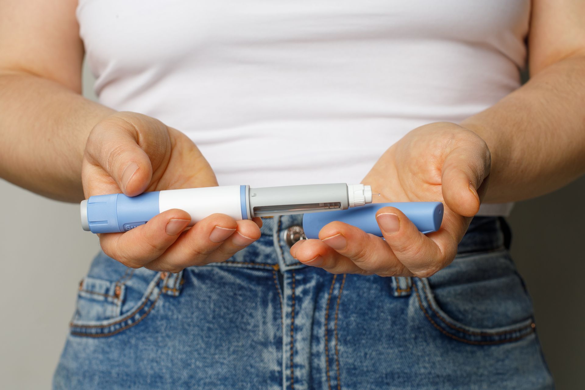 Hands holding a light blue and white insulin injection pen with its cap removed.