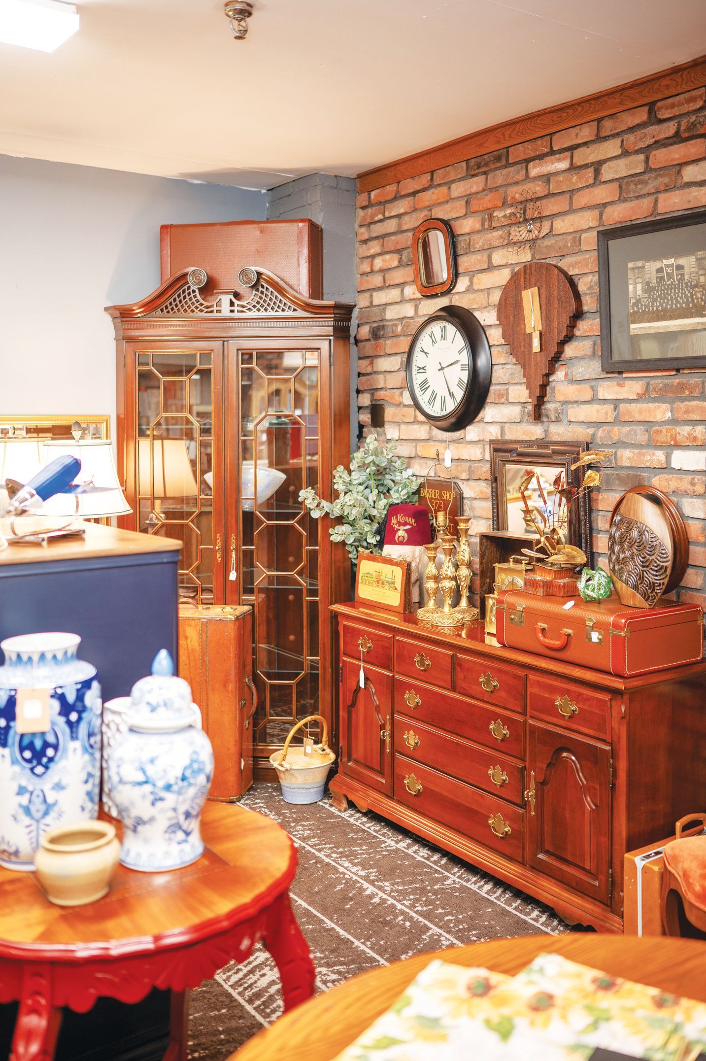 A rustic room featuring a wooden display cabinet, a brick wall with wall decor, a wooden dresser, and blue and white pottery.