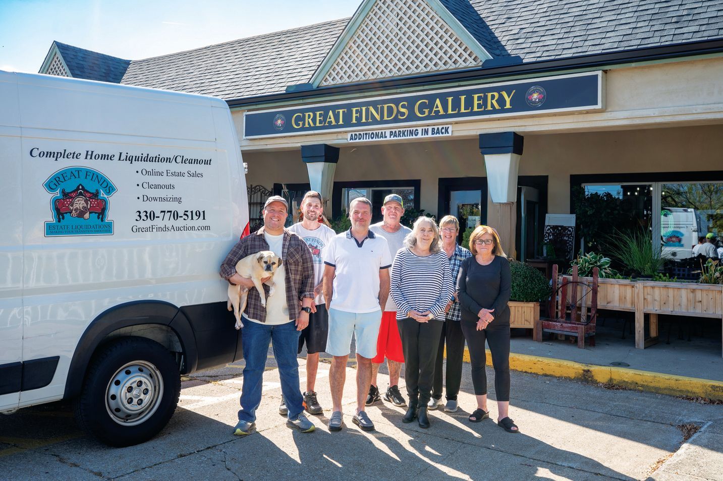 Six people and a dog stand in front of the Great Finds Gallery building next to a white service van.