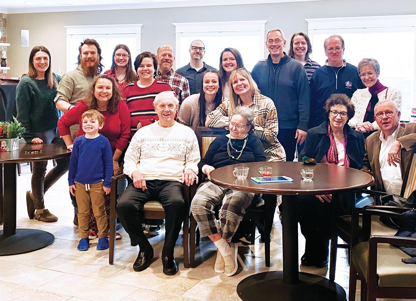 A large group of people smiling for a photo indoors, gathered around tables in a brightly lit, casual setting.