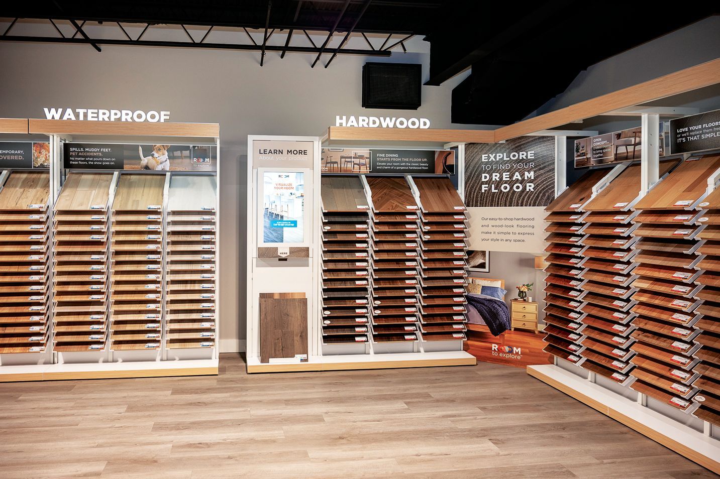 Showroom displaying various hardwood and waterproof flooring samples on organized racks under store signage.