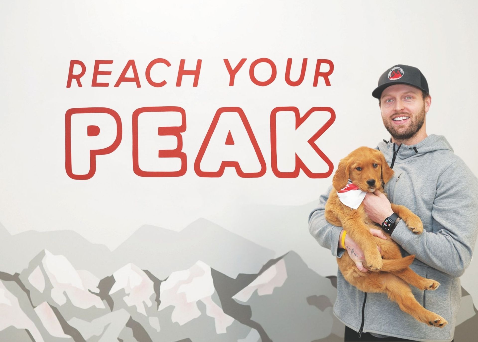 A person holds a golden puppy in front of a wall mural that reads