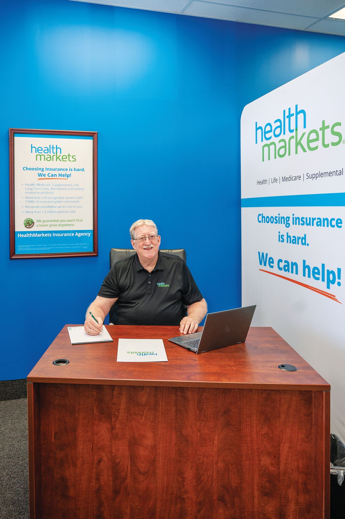 A person sits at a desk with a laptop in a HealthMarkets office with bright blue walls and branded signage.