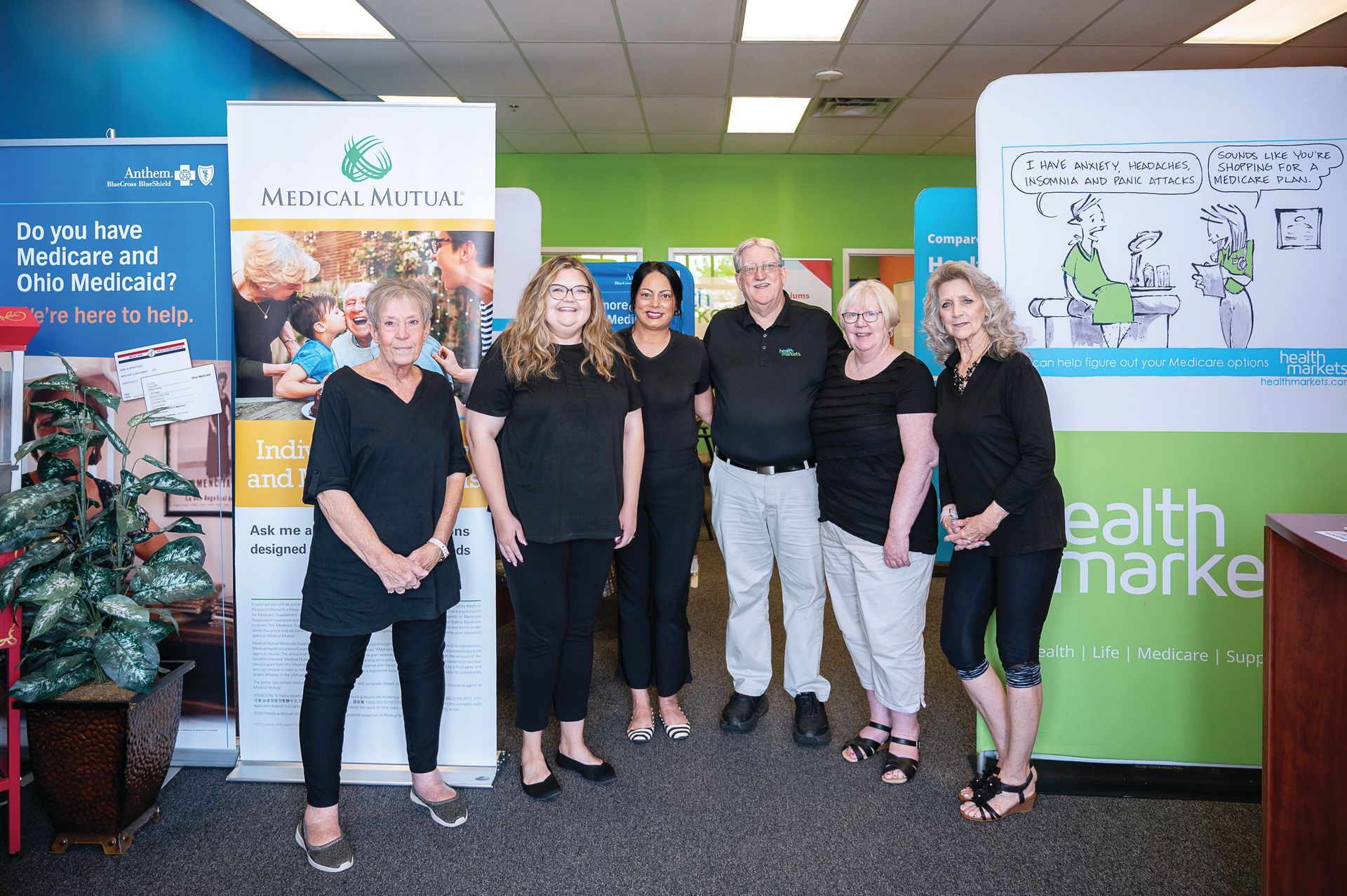 A group of six people posing in a professional office setting in front of health services display banners.