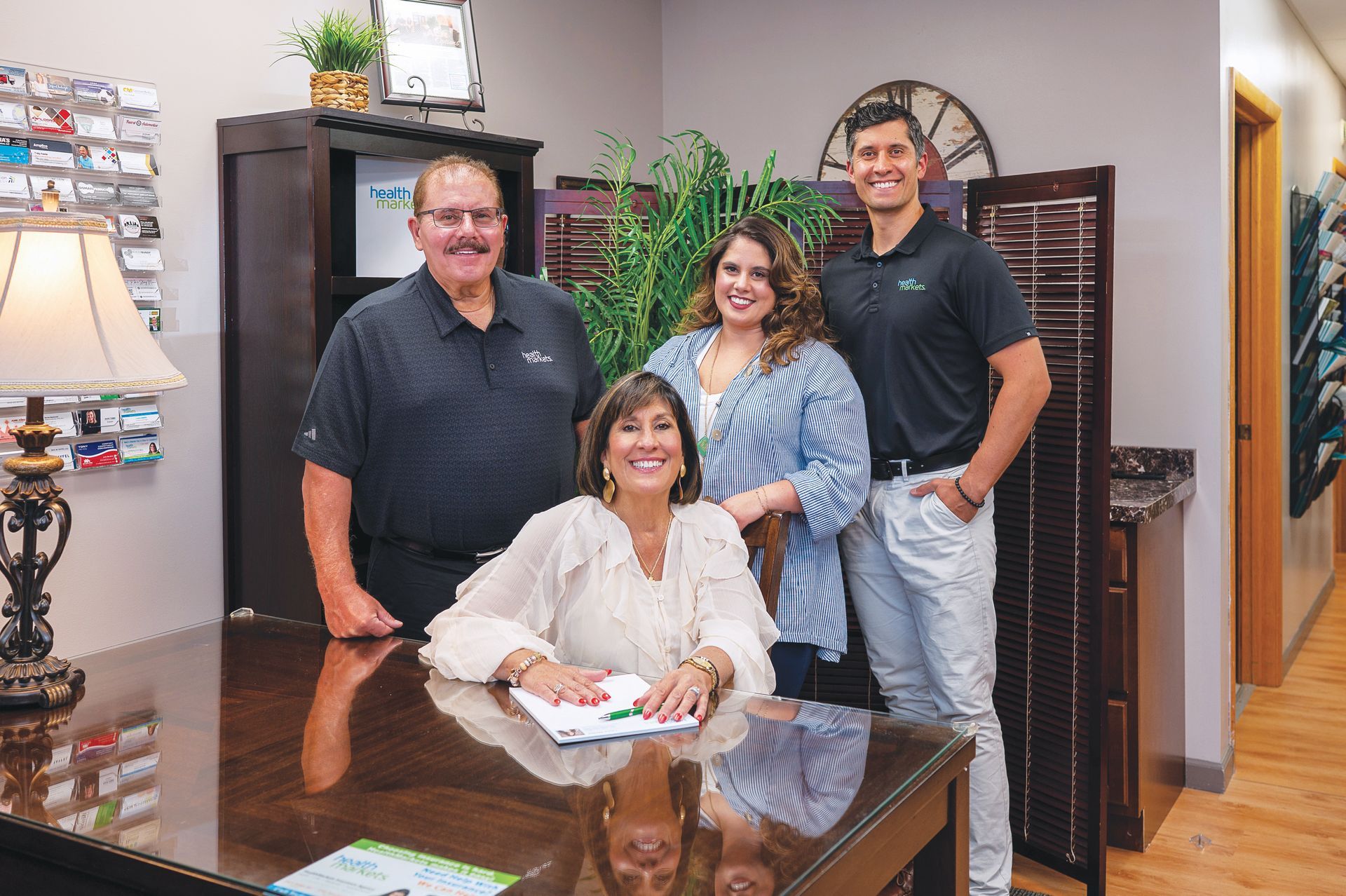 Four people posing in an office, with one seated at a desk, smiling at the camera.