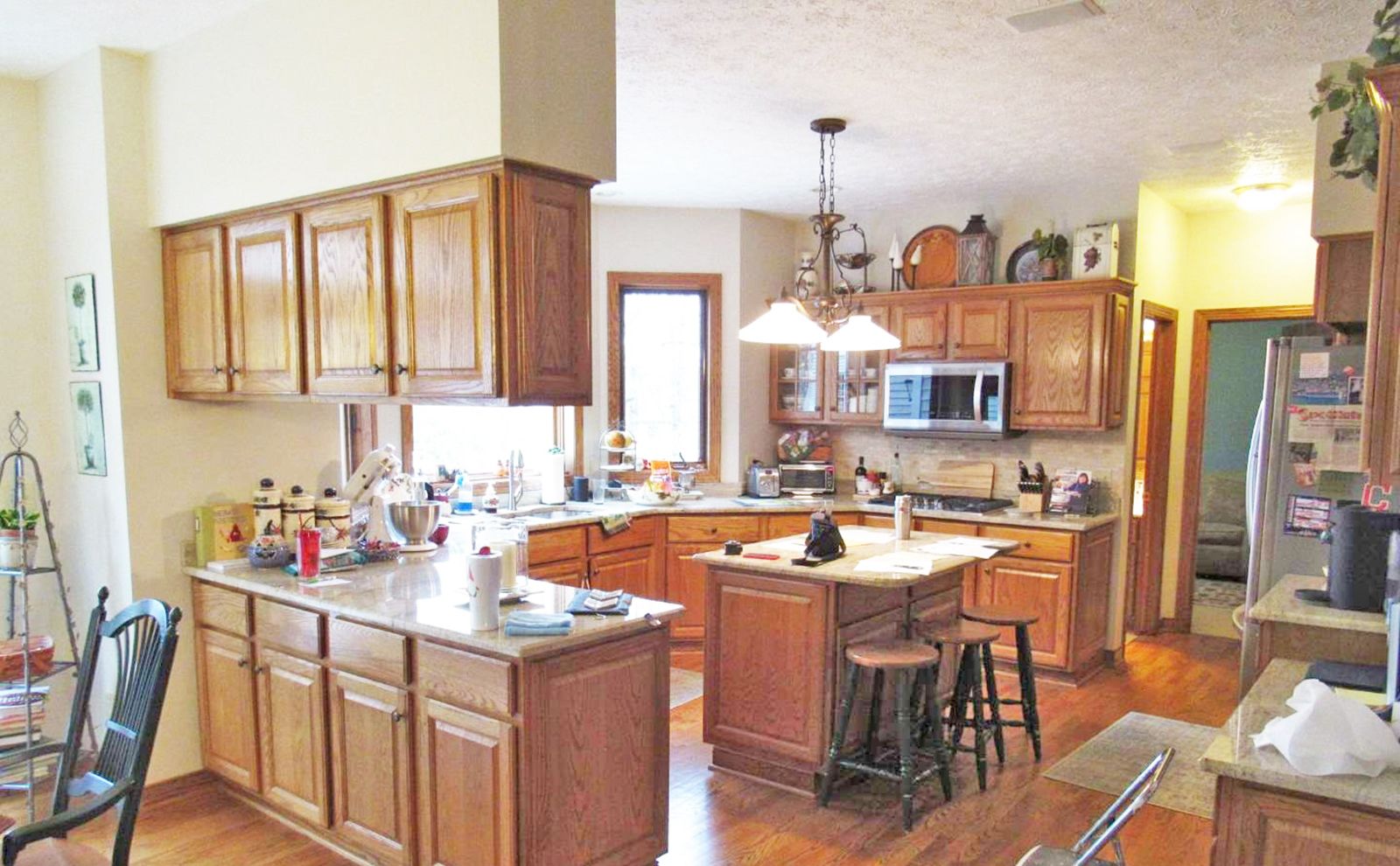 A spacious kitchen with light wood cabinets, granite countertops, a central island with stools, and stainless appliances.