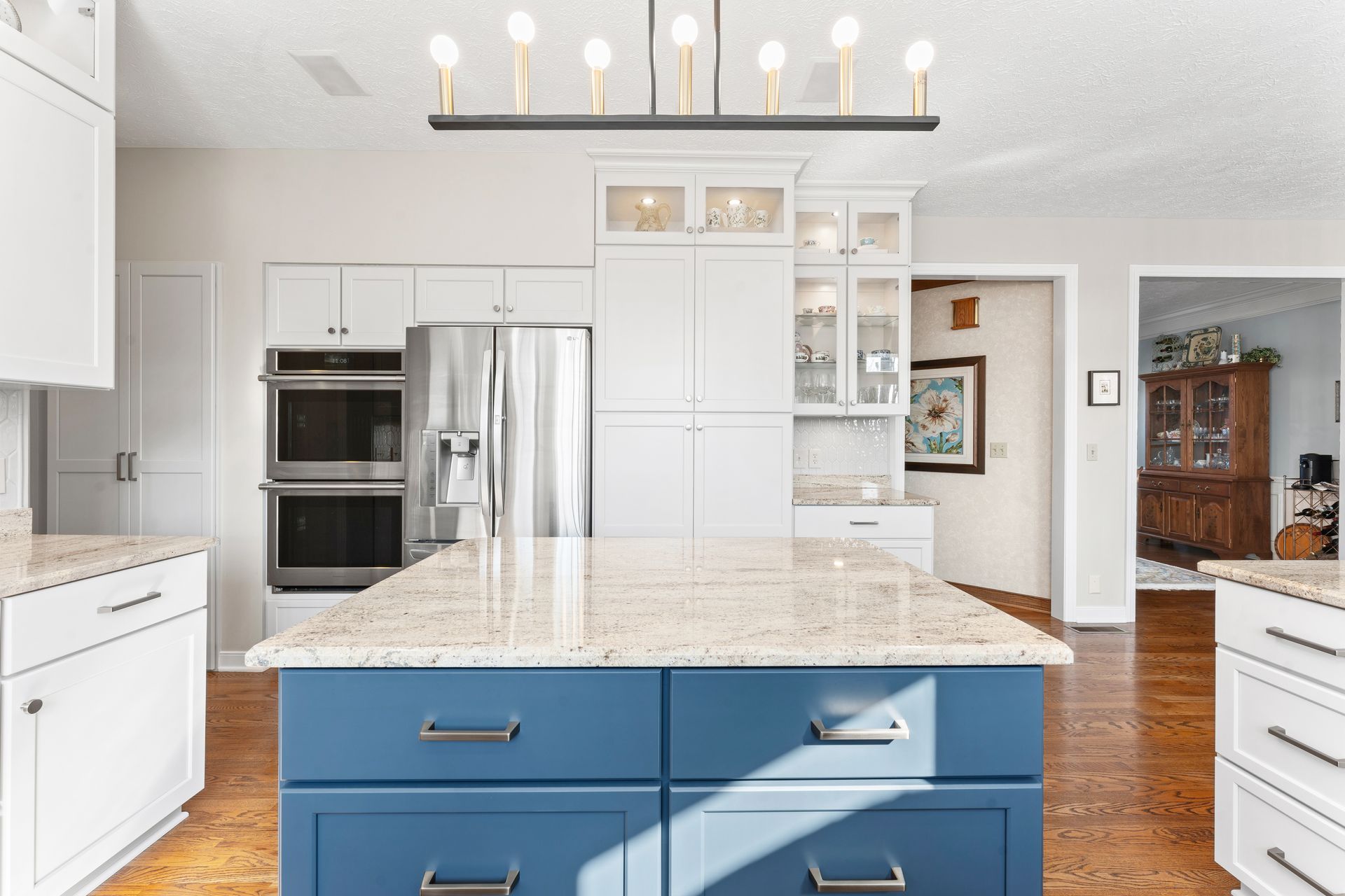 A kitchen with a blue center island, speckled granite countertops, white cabinets, stainless appliances, and a chandelier.