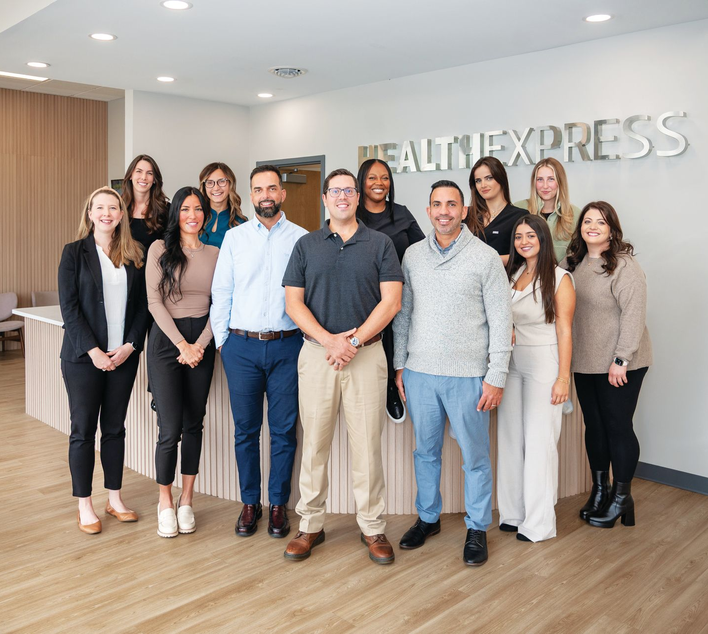A diverse team of fourteen professionals poses together in an office lobby with the Healthy Express sign on the wall.