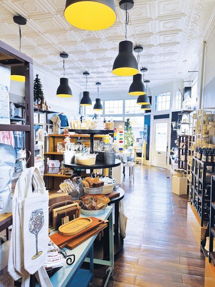 A boutique shop interior featuring wooden shelving displays, hanging yellow and black pendant lights, and patterned tile.