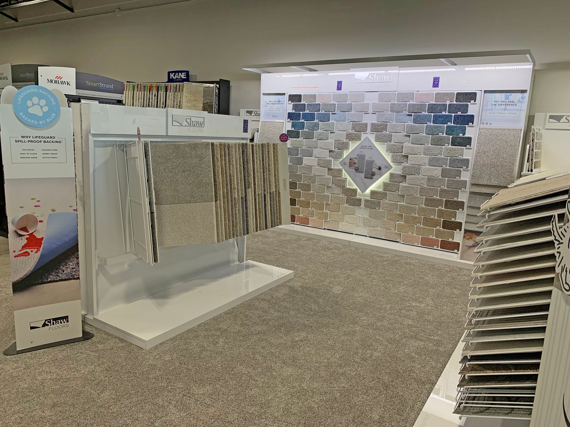 A carpet showroom display with hanging rug samples, a large wall of color swatches, and a tiered vertical rug display.