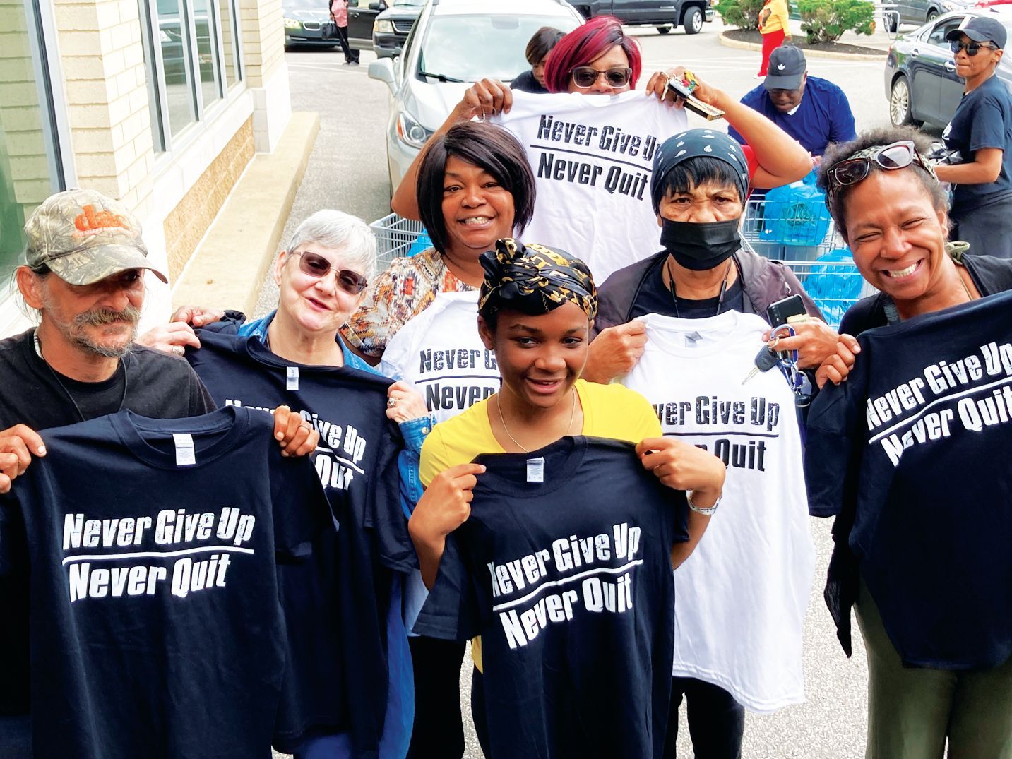 A group of people standing outdoors, holding up shirts with the slogan 