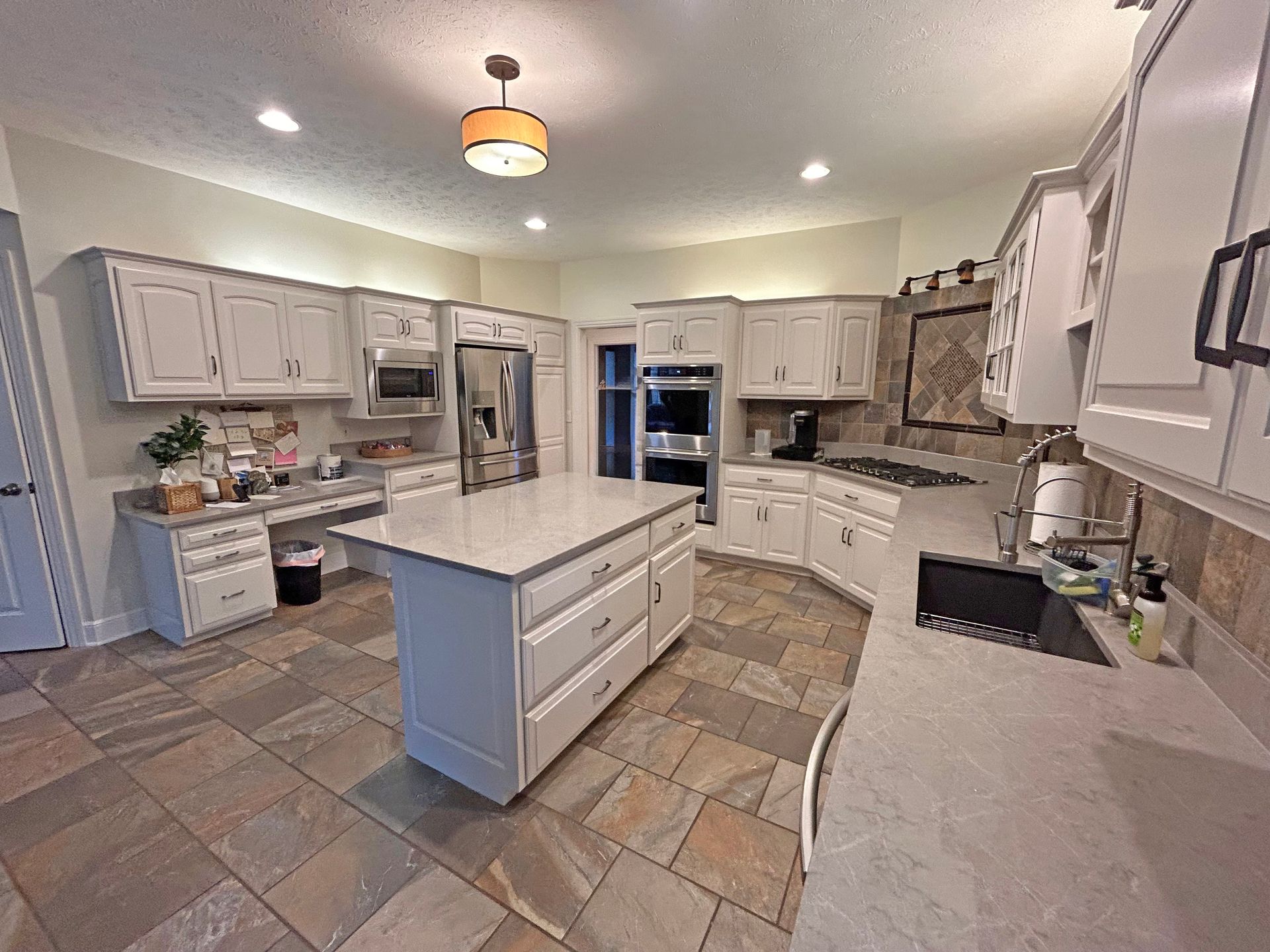 A kitchen with white cabinets, light stone tile floors, a central island with a granite countertop, and stainless appliances.