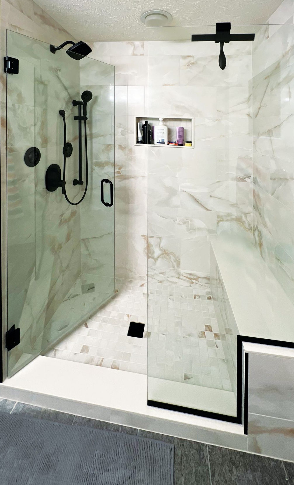 A modern walk-in shower with white marble-patterned tile, matte black fixtures, a built-in bench, and a glass door.