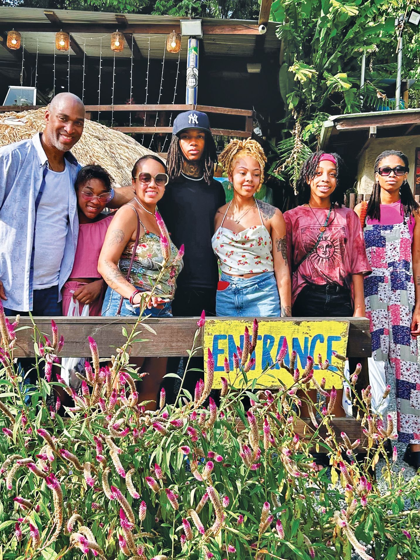 A group of seven people stands smiling behind a wooden railing with a yellow 