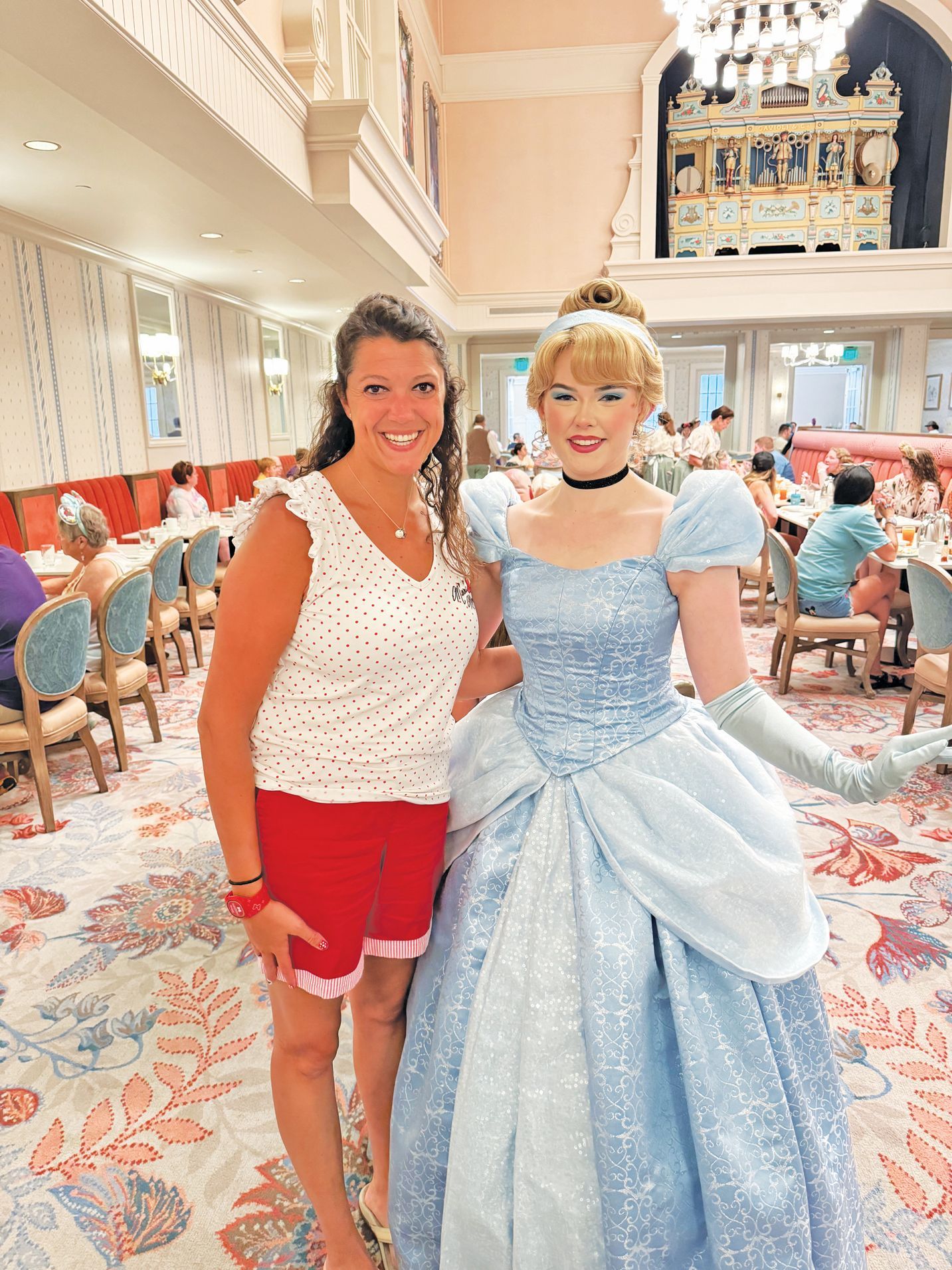 A woman smiles beside Cinderella in a blue gown at a decorated banquet hall.