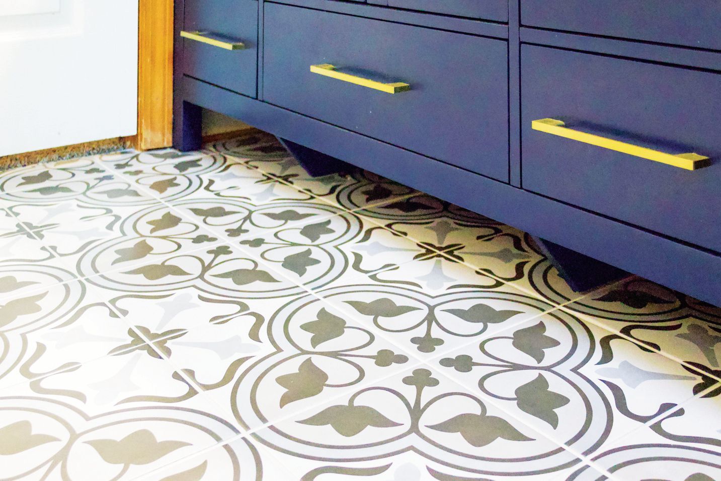 Dark blue cabinets with gold hardware are positioned above a floor tiled with a repeating gray and white floral pattern.