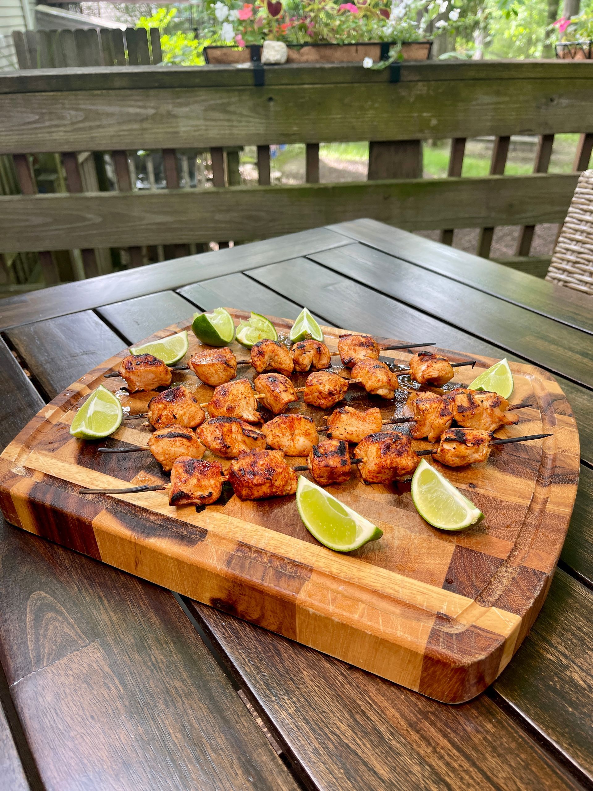 Grilled seasoned shrimp pieces served on a wooden cutting board with lime wedges on an outdoor wooden table.