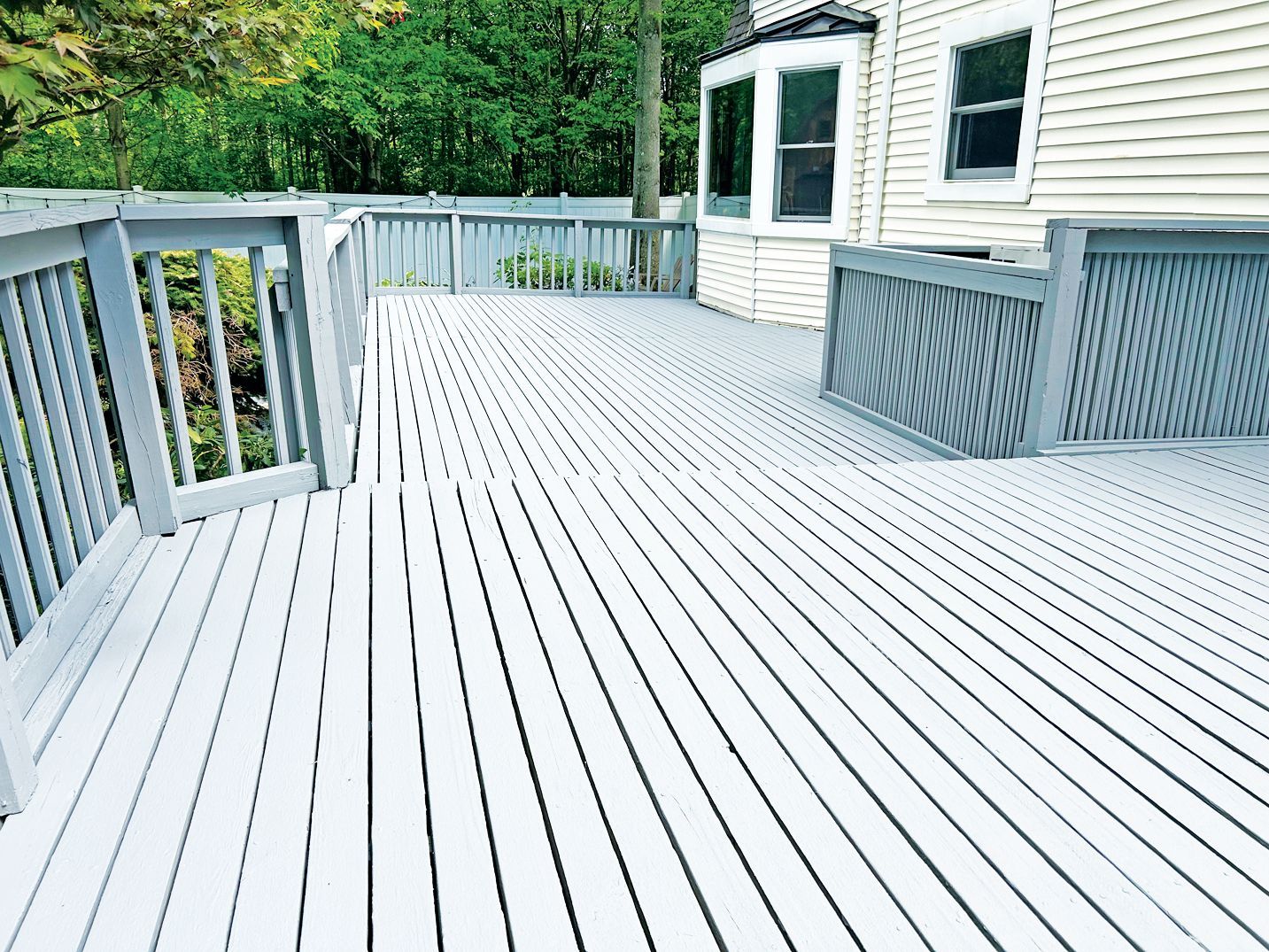 A wide-angle view of a large, light grey wooden deck attached to the side of a white house with a privacy railing.