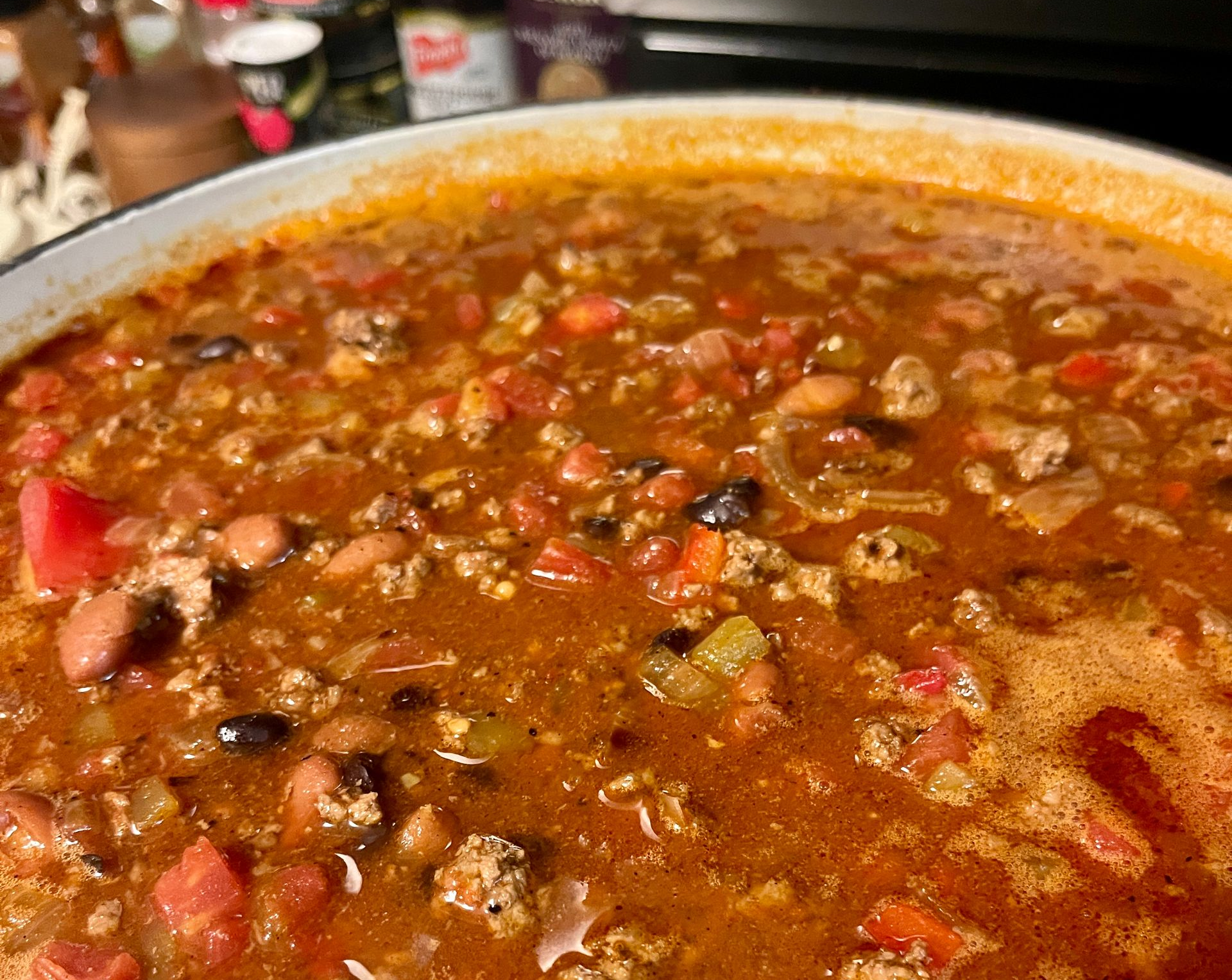 A large, close-up view of a pot filled with hearty chili, containing ground meat, tomatoes, and beans in a red sauce.