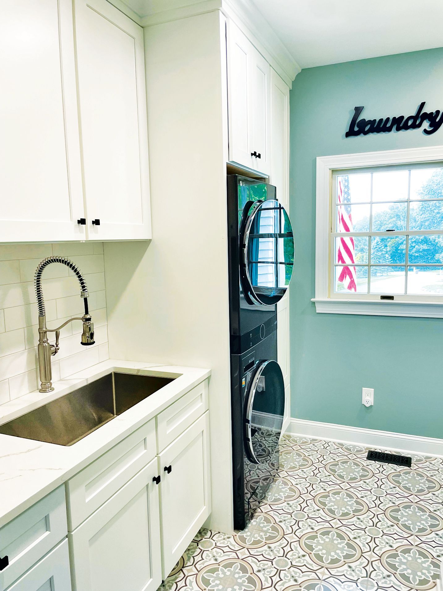A laundry room featuring white cabinetry, a sink, a stacked washer and dryer, patterned tile flooring, and teal walls.